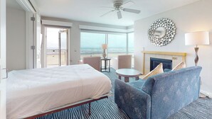 Een hotelkamer met een bed, een blauwe fauteuil, een klein rond tafeltje, een open haard en uitzicht op de oceaan.