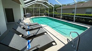 A covered outdoor swimming pool with lounge chairs and a grill. - Fabulous 4 bedroom, 3 bath home in gate community of Briarwood (Naples)