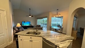 A modern kitchen with a granite countertop, white cabinetry, and a built-in dishwasher. - Fabulous 4 bedroom, 3 bath home in gate community of Briarwood (Naples)