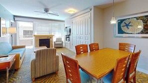 A dining area with a wooden table and chairs, a sofa, a striped armchair, and a fireplace.