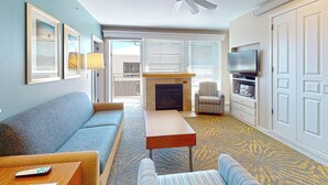 A living room with a sofa, armchair, coffee table, fireplace, TV, and a balcony with a view. - Seaside Resort - Deluxe 3 Bedroom 2 Bath - Assignment 2 (Seaside)