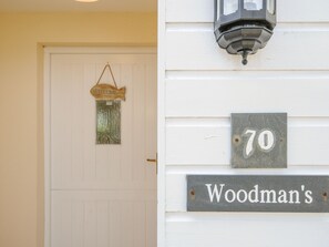 A white door with a 'WELCOME' sign and a house number '70' above a 'Woodman's' sign. - Woodmans Cottage (Falmouth)
