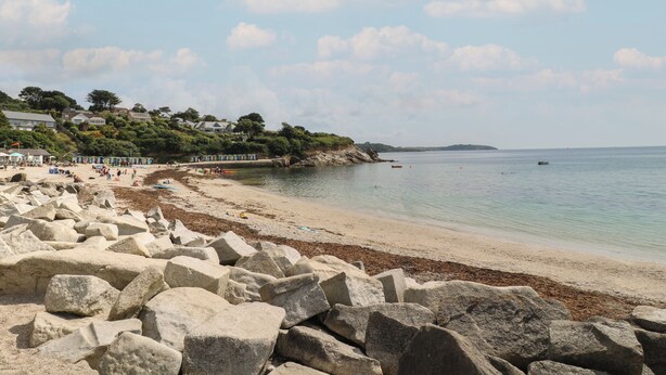 Ein Strand mit großen Felsen im Vordergrund, einem Sandufer und ruhiger See.