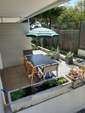 A patio with a table and chairs, a striped umbrella, and potted plants. - Studio Dans Résidence Avec Accès Direct à la Plage (Saint-Palais-sur-Mer)