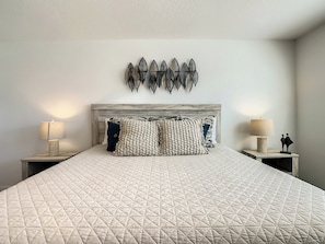 A bed with a quilted headboard, two bedside lamps, and decorative wall art.