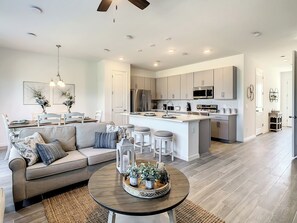 A modern kitchen with stainless steel appliances, a central island with bar stools, and a dining area with a sofa and table.