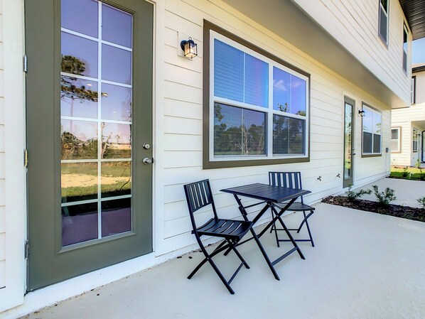 A house exterior with a sliding glass door, a patio with a table and chairs, and a window with blinds.
