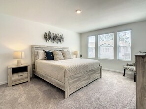 A bedroom with a bed, two bedside tables, a nightstand, a dresser, and a window with blinds.