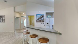 A modern kitchen with a bar area, white cabinetry, and a painting of palm trees. - Coastal Home, Close to Beach with Pool, Golf Cart and Bikes (Miramar Beach)