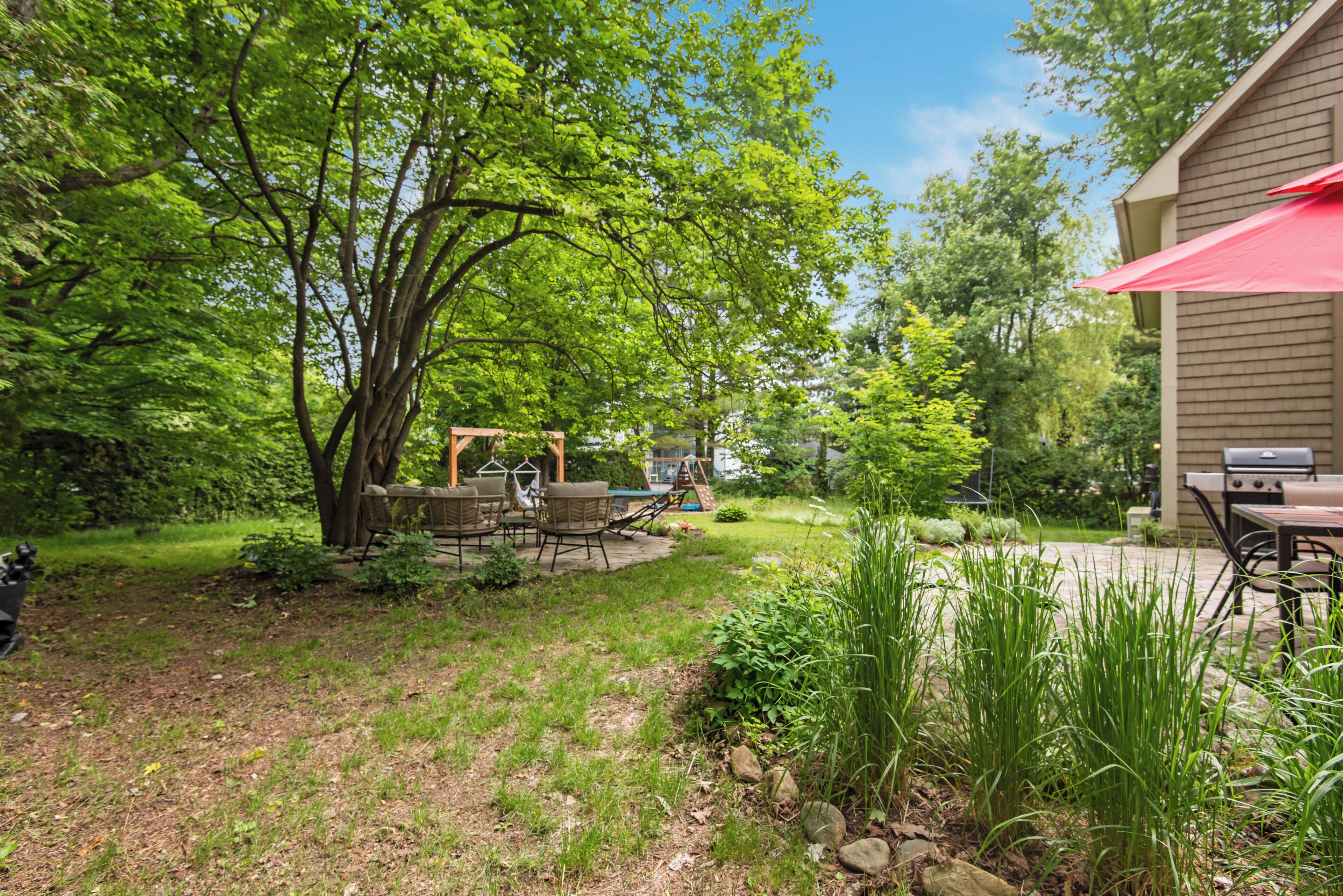 A backyard with a patio, outdoor furniture, a swing set, and a barbecue grill.