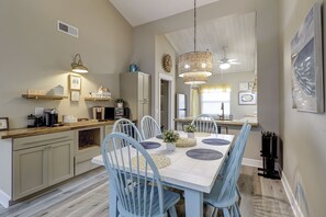A modern kitchen with light blue chairs, a dining table, and a hanging light fixture. - Sunset Rentals | Treetops 7802 | Dog Friendly (Hilton Head Island)