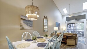 Zona pranzo con tavolo bianco, sedie blu e lampadario in vimini.