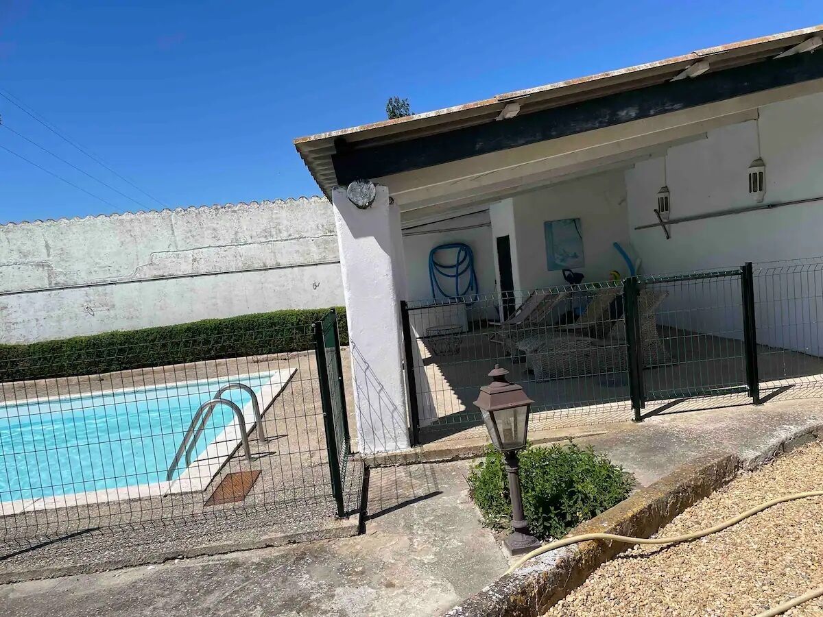 A swimming pool with a fence, a building with a white exterior, and a small garden area with a lamp post.