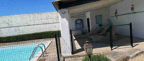 A swimming pool with a fence, a building with a white exterior, and a small garden area with a lamp post.