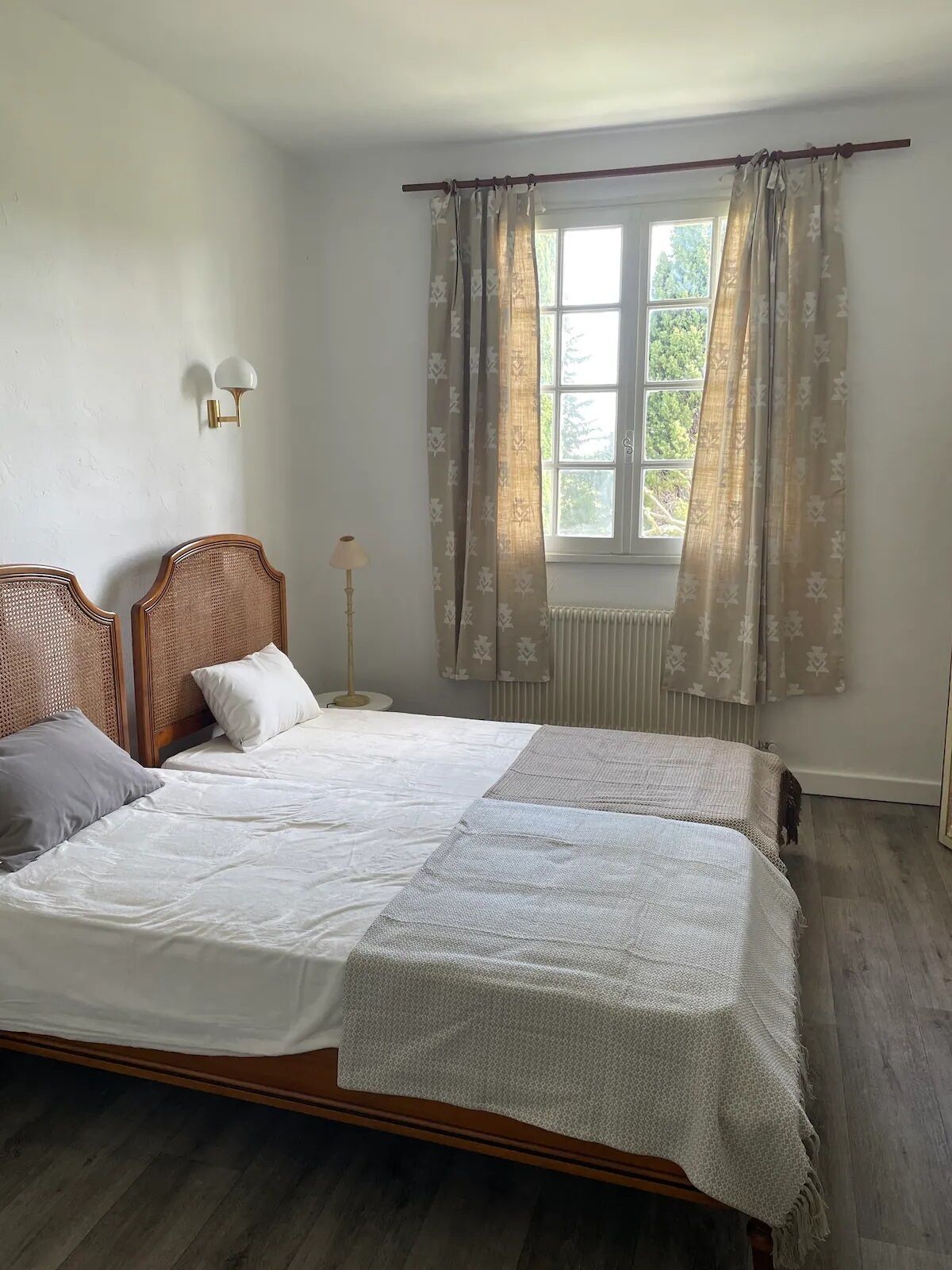 A double bed with a wooden headboard, two bedside tables, a floor lamp, and a window with curtains.