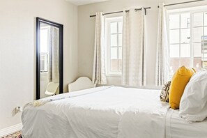 Une chambre à coucher avec un lit, une chaise, une fenêtre avec des rideaux et un miroir.