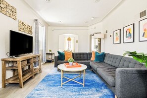 Ein Wohnzimmer mit Flachbildfernseher, einer Couch, einem Couchtisch und einem blauen Teppich.