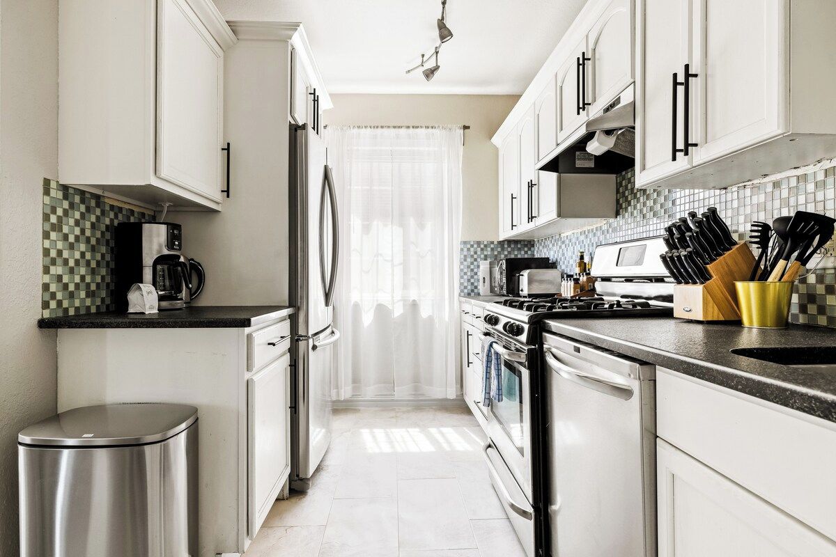 A modern kitchen with white cabinets, a stainless steel trash bin, and a coffee maker.