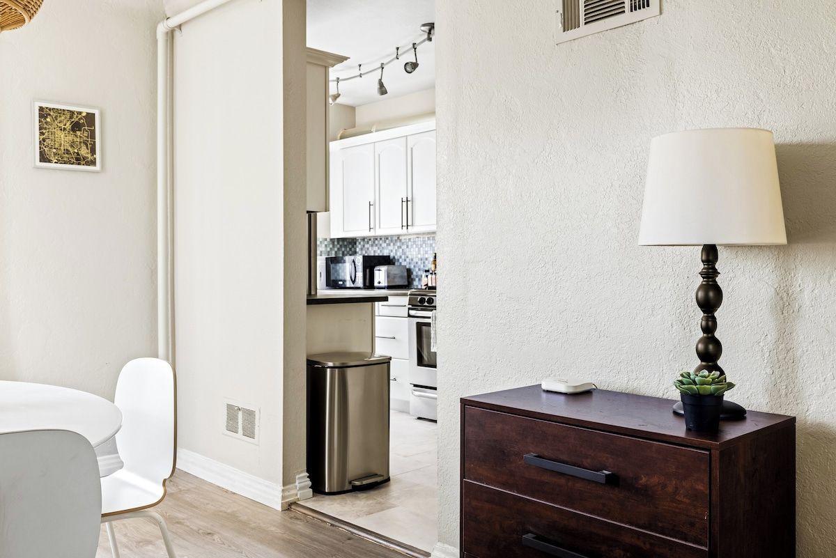 Una cocina moderna con armarios blancos, electrodomésticos de acero inoxidable y un comedor con mesa y sillas blancas.