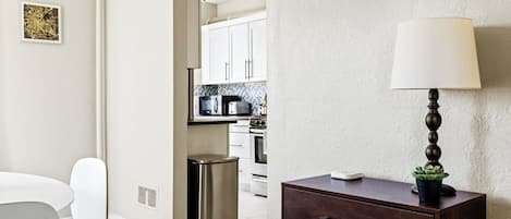 Una cocina moderna con armarios blancos, electrodomésticos de acero inoxidable y un comedor con mesa y sillas blancas.