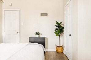 Ein Schlafzimmer mit einem Bett, einem Schminktisch, einer Topfpflanze und einer Tür.
