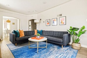 Un salon moderne avec un canapé d’angle, une table basse ronde et un tapis à motifs bleus.