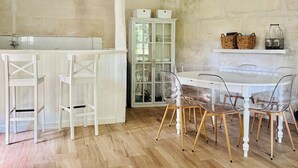 A kitchen with white cabinetry, a wooden floor, and a dining area with clear chairs and a white table. - Les Aulnes - Two Bedrooms - Five people (Mosnac-Saint-Simeux)