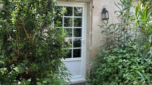 A garden with a white door, a stone wall, and various green plants. - Les Aulnes - Two Bedrooms - Five people (Mosnac-Saint-Simeux)