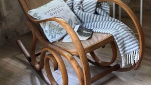 A wooden rocking chair with a striped throw blanket and a pillow with botanical print, positioned near a window with a view of greenery. - Les Aulnes - Two Bedrooms - Five people (Mosnac-Saint-Simeux)