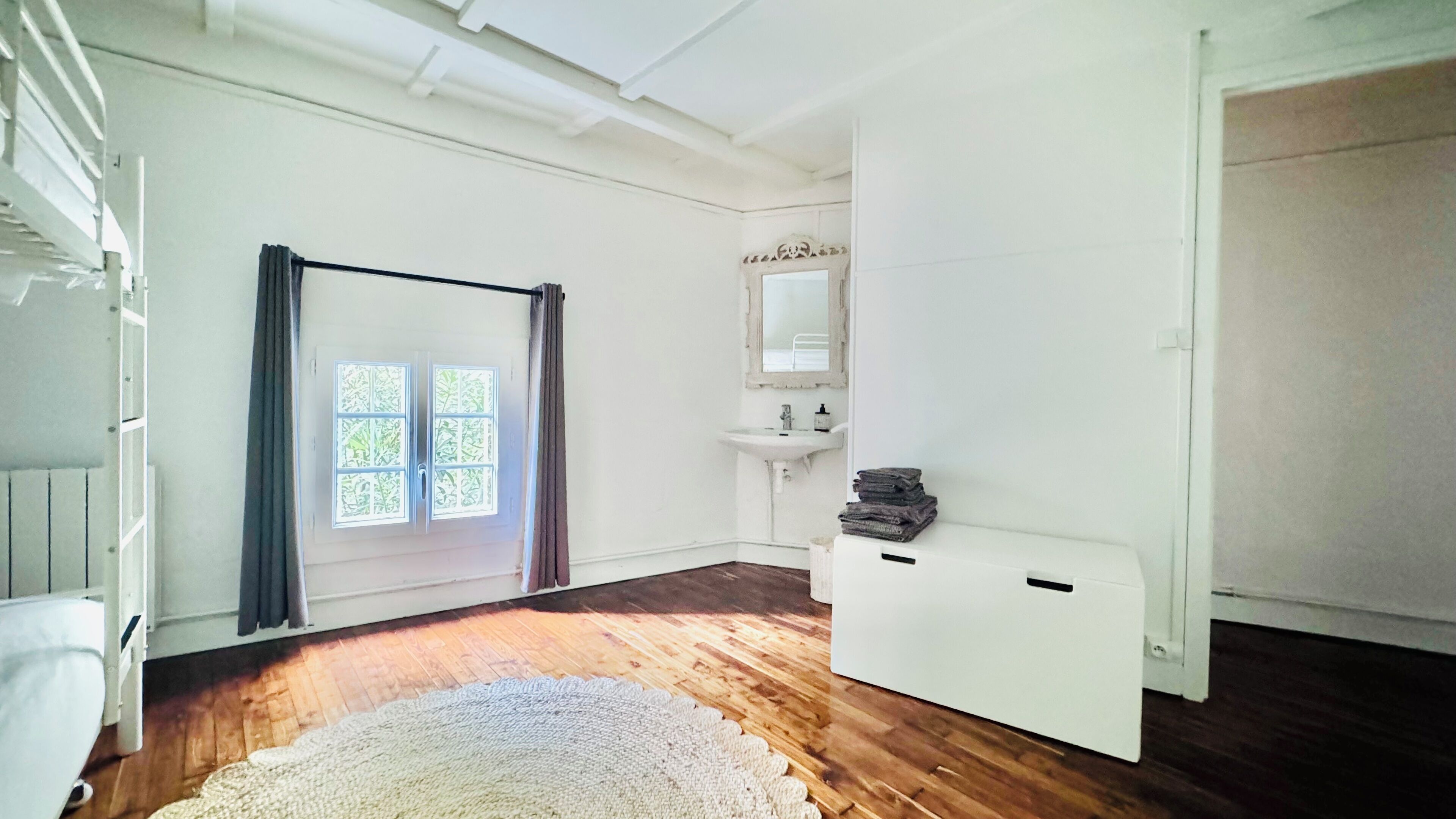 Una habitación con un ventanal grande, un radiador blanco, un lavabo y un armario blanco.