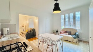 A modern kitchen with a gas stove, a dining area with a white table and chairs, a cozy seating area with a sofa and cushions, and large windows providing natural light.