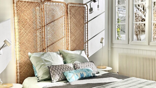A bedroom with a bed, bedside tables, a window with blinds, and a radiator.