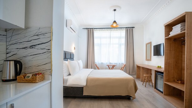 Una habitación de hotel con cama, escritorio, televisor, armario y una pequeña kitchenette.
