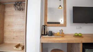 Una estantería de madera con un perchero, una tetera, una taza, una cesta con aperitivos y dos manzanas sobre una encimera de madera.