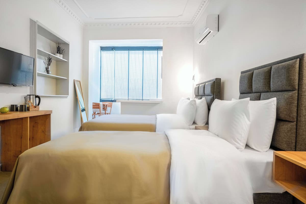 Ein Hotelzimmer mit zwei Betten, einem Fernseher, einem Fenster mit Jalousien und einem Holztisch.