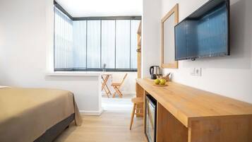 Een moderne slaapkamer met een bed, een houten bureau, een televisie en een raam met zonwering.