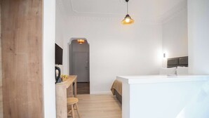 Una habitación de hotel moderna con piso de madera, una cama blanca, un escritorio pequeño con una silla y una lámpara colgante.