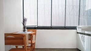 Una cocina con una mesa de comedor, sillas, un florero con flores secas y una ventana con persianas.