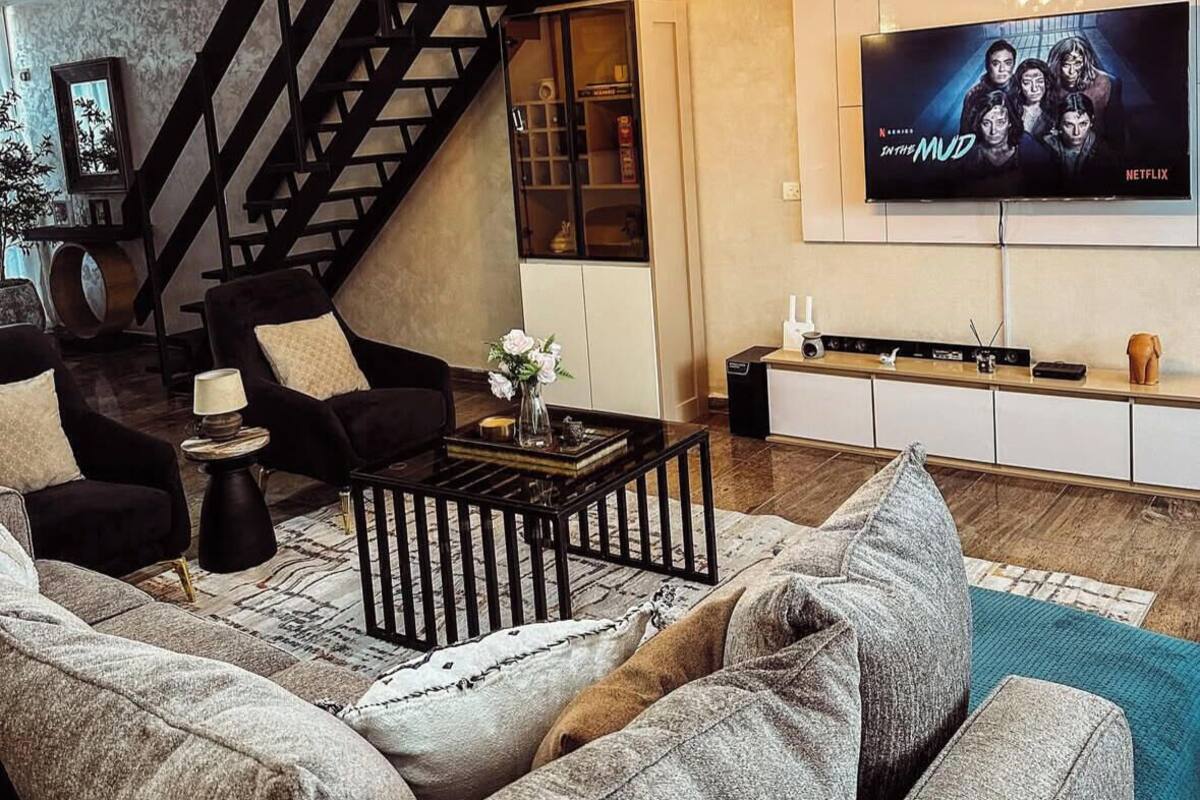 Un salon moderne avec un escalier noir, un grand téléviseur et un coin salon confortable.
