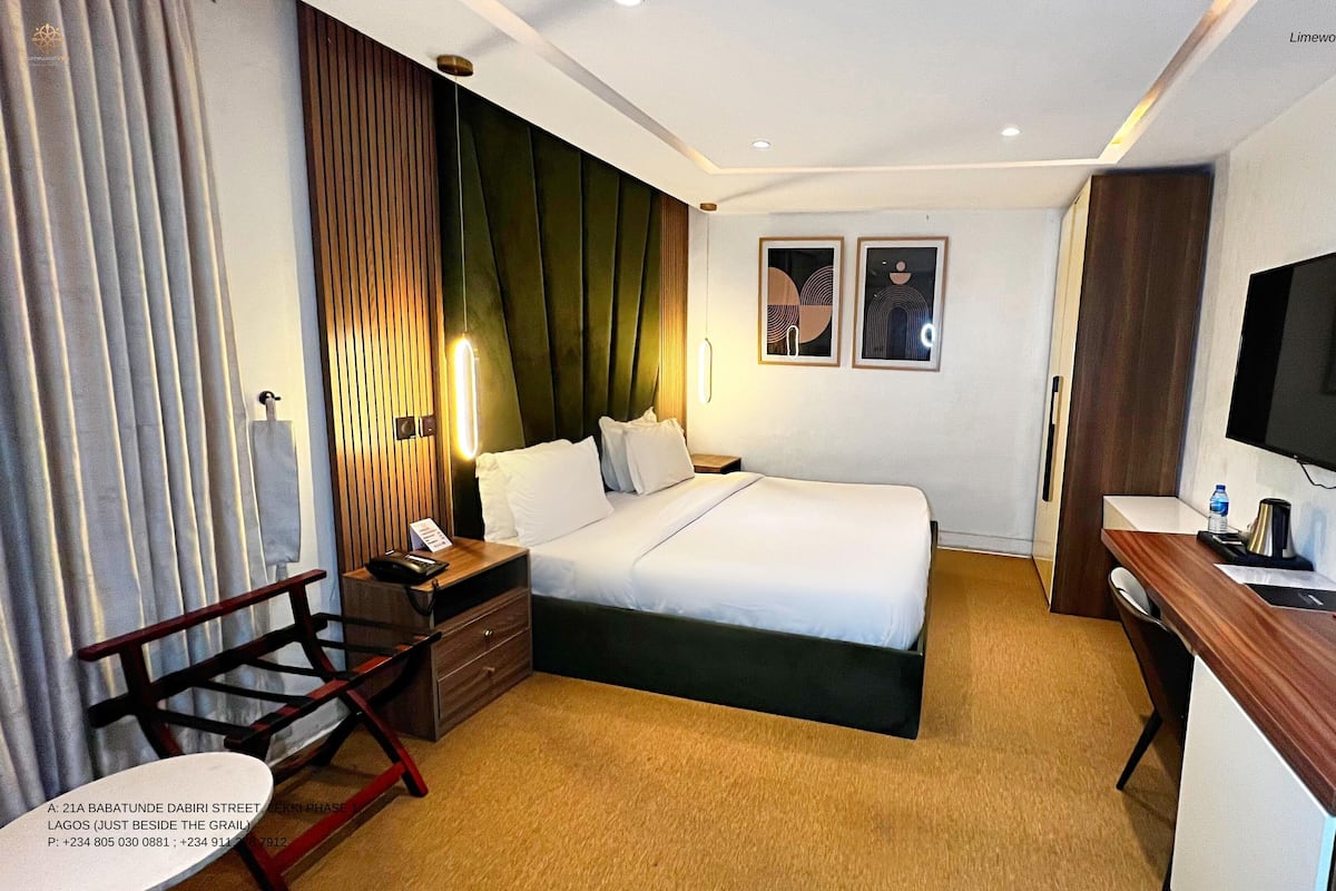 Une chambre d’hôtel comprenant un lit, une table de chevet, une lampe, une télévision, un bureau, une chaise et donnant sur la rue.