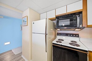 Kitchen area with refrigerator, microwave, and stove, set against light blue walls and wooden flooring.
