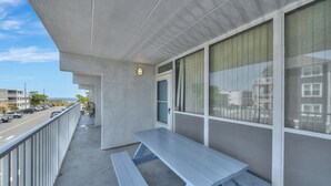 Un balcón con mesa y bancos de madera, vista a la calle y un edificio con ventanas amplias.