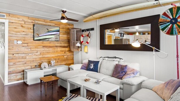 Una sala de estar moderna con una pared de madera, muebles blancos, un ventilador de techo, un espejo grande y un dardo.