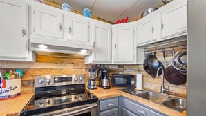 Una cocina con gabinetes blancos, estufa, microondas y pileta.
