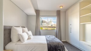 A modern hotel room with a large bed, a wardrobe, and a view of the cityscape.
