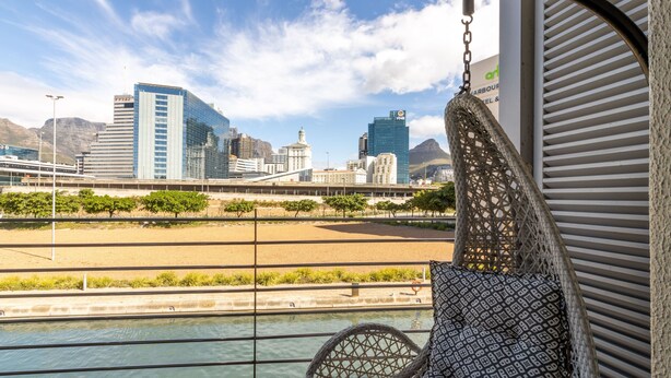 A view from a balcony with a hanging chair overlooking a river, a cityscape with modern buildings, and a sign for a restaurant.