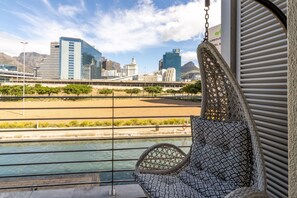A view from a balcony with a hanging chair overlooking a river, a cityscape with modern buildings, and a sign for a restaurant. - Experience Uninterrupted Comfort Fully Furnished 2br Flat Free From Loadsheding (Cape Town)