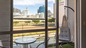 A balcony with a hanging chair, a round table, and a view of a cityscape including a bridge and buildings.