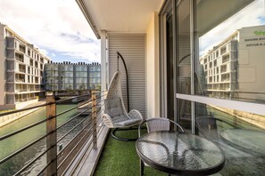 A balcony with a glass table, a wicker chair, and a view of a river and buildings.