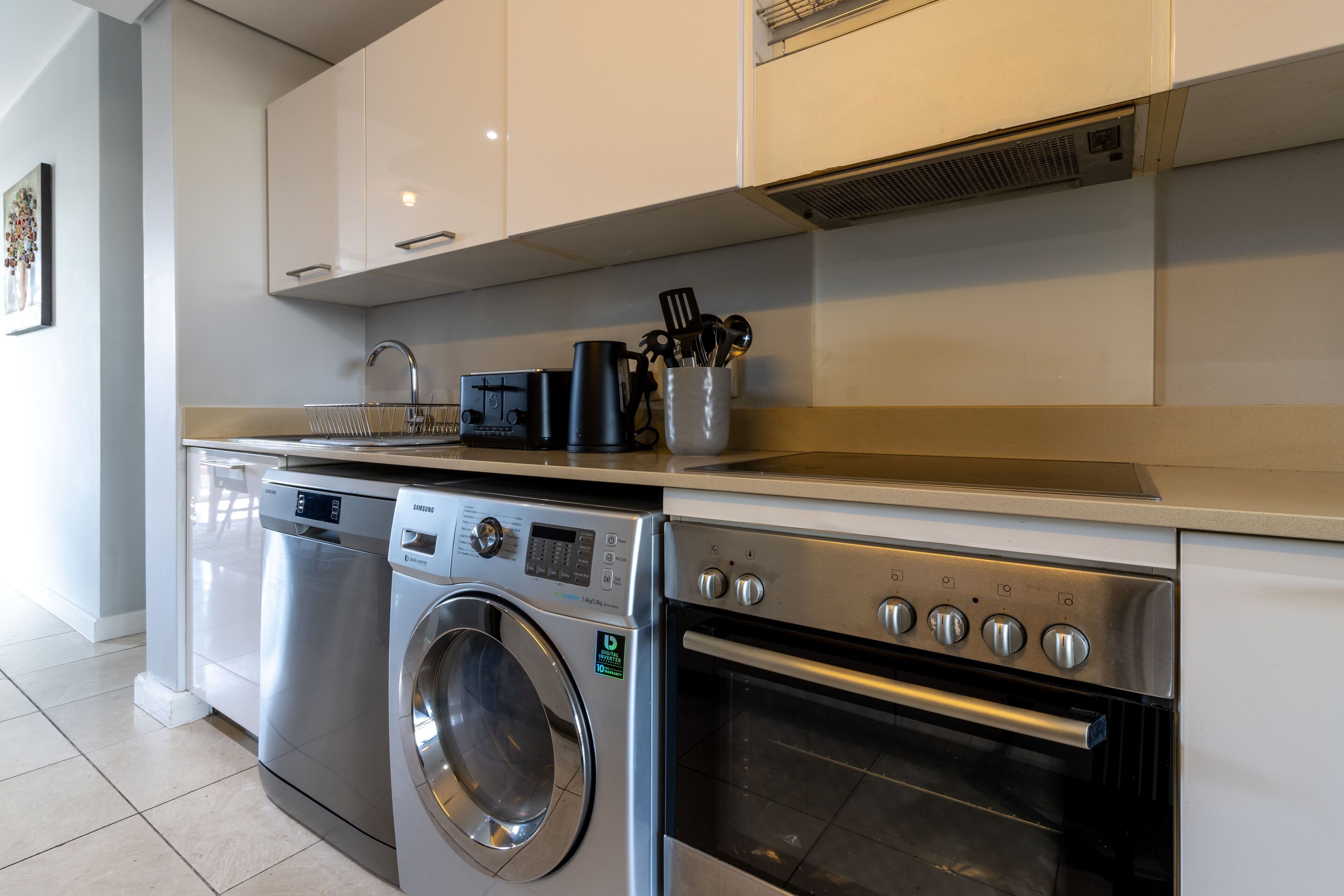 A modern kitchen with a stainless steel dishwasher, a front-loading washing machine, and a built-in oven.